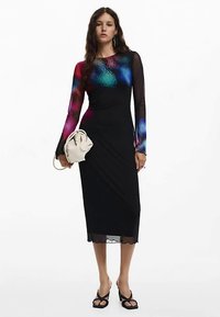 Svart midiklänning med långa genomskinliga ärmar, färgglatt abstrakt mönster på livet, vågformad fåll, ihop med en krämfärgad väska och svarta sandaler.