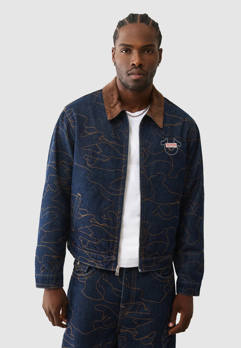 Spijkerjack met een bruine corduroy kraag, blauwe stof met een oranje abstract patroon en een ritssluiting aan de voorkant.