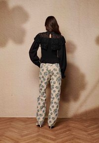 Blouse noire avec un jeu de dentelle et un corps froncé, associée à un pantalon crème orné de motifs floraux bleus. Conception longue jusqu'au sol et ajustée.