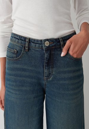 Dunkelblaue Denim-Jeans mit Reißverschluss, fünf Taschen und sichtbarem Bundknopf. Der Stoff hat eine sichtbare Textur und leichte Verfärbungen.