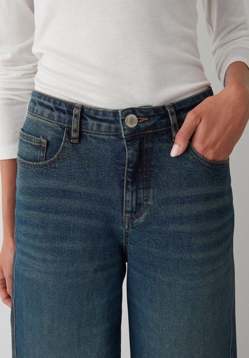 Dark blue denim jeans with a zipper fly, five pockets, and a visible top button. The fabric has a visible texture and slight fading.