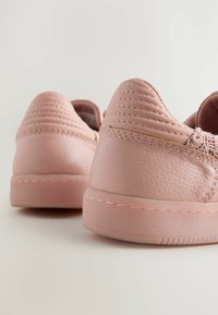 Rosa sneakers med en texturerad läderövre, med randig detaljer vid hälen och en slät gummisula.