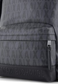 Zaino nero con un motivo testurizzato e un fondo in pelle liscia. Tasca con zip dotata di una linguetta con marchio e dettaglio con logo impresso.