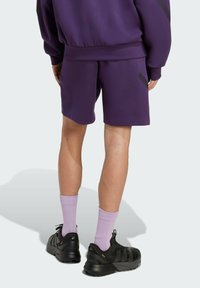 Fialové sportovní šortky s volným střihem, doplněné o levandulové ponožky a černé tenisky. Šortky mají hladkou texturu a minimalistický design.