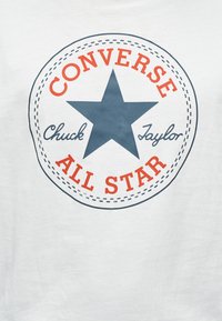 T-shirt en coton blanc avec un graphique rond représentant une étoile bleue, le texte rouge « CONVERSE » au-dessus, et les mots « CHUCK TAYLOR » et « ALL STAR » en texte incurvé en dessous.