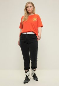T-shirt in cotone arancione con dettagli grafici, abbinato a jeans neri e stivaletti a fantasia bianco e nero. Fit casual con risvolti sulle maniche.
