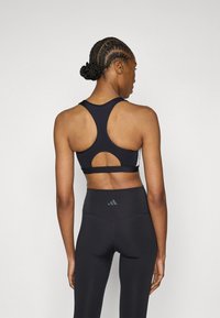 Μαύρο αθλητικό σουτιέν με σχέδιο racerback και λεπτομέρεια κοψίματος, σε συνδυασμό με μαύρο κολάν ψηλόμεσο με λεπτομέρεια λογότυπου στο πίσω μέρος.