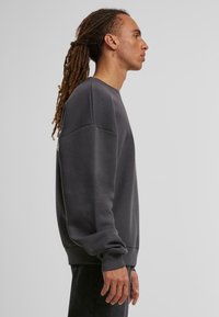 Mørkegrå sweatshirt med en afslappet pasform, sænkede skuldre, ribbede manchetter og en glat overflade, vist på en model fra siden.