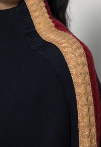 Pull en tricot avec un corps noir, mettant en vedette des accents texturés dorés et bordeaux le long des épaules et un col côtelé.