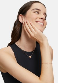 Smykker i rosaguld, der inkluderer en hjerteformet vedhængsnekke og matchende armbånd. Glat overflade med et delikat kædedesign.