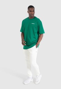 Grünes Baumwoll-T-Shirt mit Rundhalsausschnitt und kurzen Ärmeln, kombiniert mit weißen Jogginghosen und weißen Sneakers.