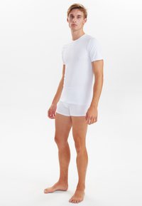 White cotton blend t-shirt with short sleeves and crew neck, paired with white boxer briefs. Smooth texture, fitted design, minimal seams.