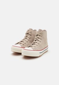Zapatillas altas beige de ante con puntera blanca, suela de goma texturizada y acentos en rojo y azul en la entresuela.