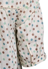 Blusa de manga corta en tejido ligero, con base color crema y lunares multicolores en marrón, verde azulado y menta. Detalle de puño visible.