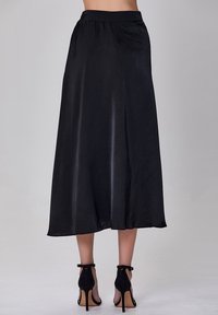 Jupe midi en satin noir avec une taille élastique, une forme fluide et une texture lisse, associée à des talons à sangle de cheville noirs.