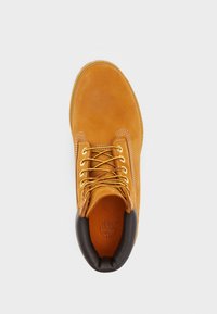 Botte en daim marron avec un bout rond, des lacets jaunes et un col rembourré noir. Dotée d'une semelle intérieure texturée et du logo embossé à l'intérieur.