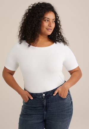 T-shirt bianco a maniche corte con scollo rotondo, abbinato a jeans a vita alta blu scuro, che mette in risalto un design attillato e una struttura liscia.