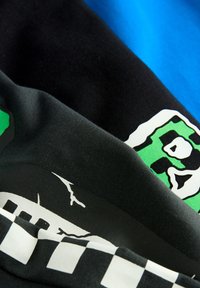 Tissu de t-shirt en coton bleu, noir et vert, avec des impressions graphiques, y compris des accents blancs et un motif à carreaux.