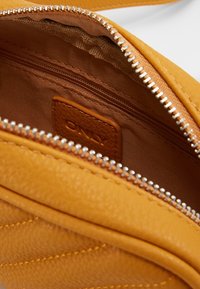 Intérieur d'un sac en cuir jaune avec une texture lisse et un tissu doublé. Comprend une poche zippée et une étiquette cousue marron.