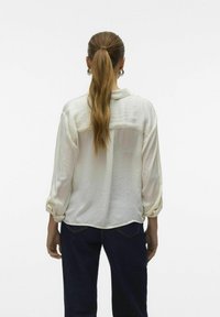 Blusa bianca leggera con vestibilità morbida, maniche a toppa e una leggera lucentezza. Abbinata a jeans in denim scuro, visualizzata da dietro.