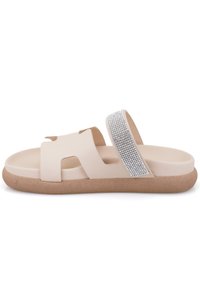 Sandale glissante beige avec deux larges brides, l'une ornée de strass en argent, et une semelle brune texturée pour l'adhérence.