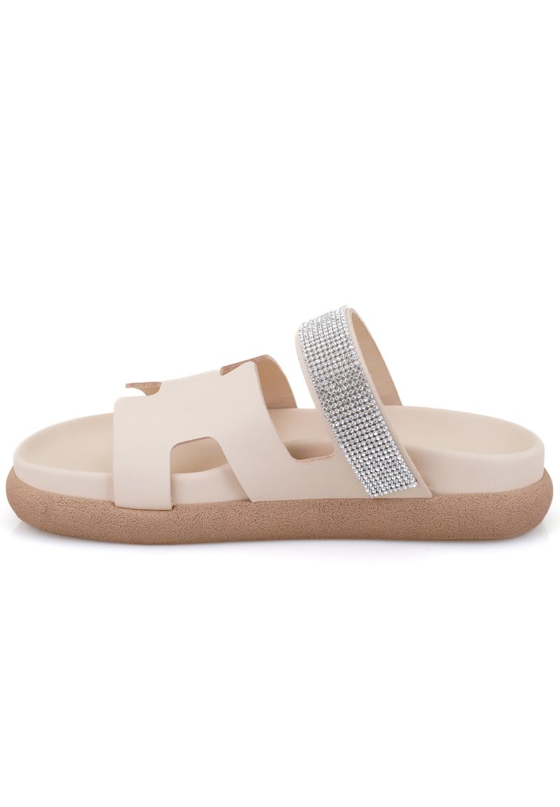 Sandale glissante beige avec deux larges brides, l'une ornée de strass en argent, et une semelle brune texturée pour l'adhérence.