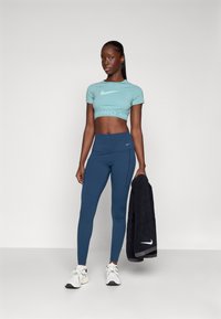 Top deportivo corto de color azul claro con el logo de Nike, combinado con leggings de tiro alto de color azul oscuro y zapatos deportivos blancos. Sosteniendo una toalla oscura.