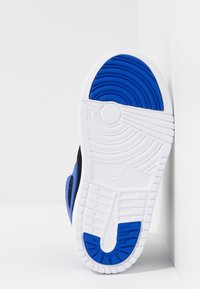 Černá podrážka tenisky s modrými a bílými akcenty, s texturovanými vzory a kruhovým logem. Zakřivený design s drážkami pro trakci.