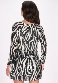 Zwart en crème jurk met lange mouwen, voorzien van een golvende zebra print en een getailleerde taille, gemaakt van een lichtgewicht, doorschijnende stof.