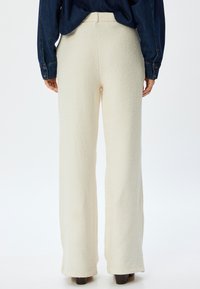 Pantalones de pierna ancha en color crema, hechos de tela texturizada. Diseño de cintura alta con una cinturilla suave. Detalles de costura visibles y dobladillo acampanado.