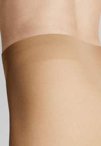 Beige Strumpfhose mit einer glatten Textur und weichem, elastischem Bund, der eine semi-opake Erscheinung aufweist und in einen hautfarbigen Farbton übergeht.