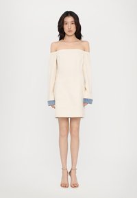 Rochie crem cu umerii descoperiți, cu mâneci lungi și manșete din denim. Material neted, design ajustat și lungime până deasupra genunchilor. Stil minimalist.