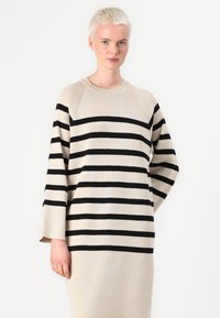 Beige genser med svarte horisontale striper, med rund hals og lange ermer, laget av et mykt strikkemateriale.