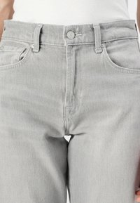 Jeans en denim gris clair à taille haute, avec cinq poches, une fermeture à bouton et des détails de couture subtils sur le pantalon.