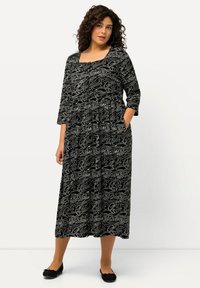 Musta-valkoinen kuviollinen mekko, jossa on kolme neljäslähtöä hihat, pyöreä kaula-aukko, taskut ja virtaava maxi-siluetti. Pehmeä kankaan tekstuuri.