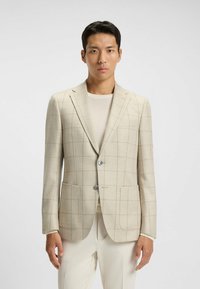 Beige rutigt blazer i texturerat tyg med två framfickor och en enkel knappstängning; kombinerat med en ljus topp och byxor.