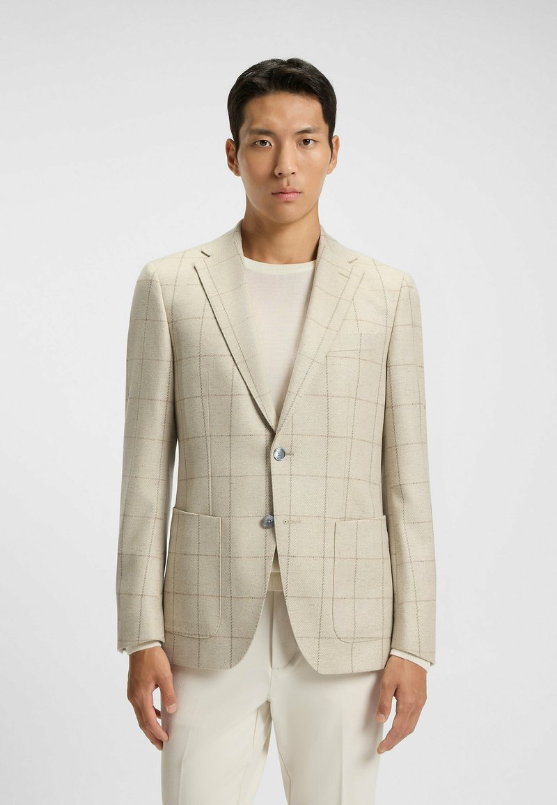 Beige rutigt blazer i texturerat tyg med två framfickor och en enkel knappstängning; kombinerat med en ljus topp och byxor.
