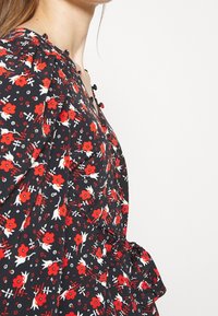 Robe noire à fleurs avec des fleurs rouges et des accents blancs, dotée de boutons et d'une taille peplum. Tissu texturé avec une coupe décontractée.