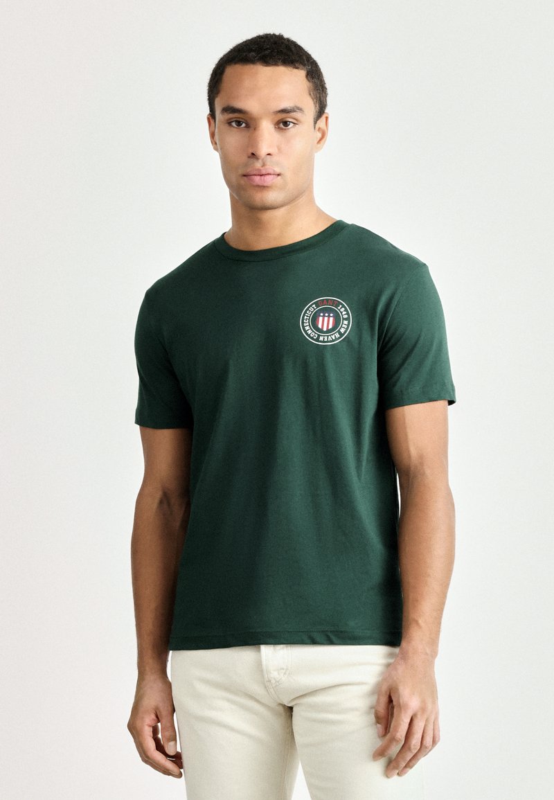 Grøn bomulds T-shirt med rund hals, korte ærmer og et rundt logo på brystet. Stoffet ser glat ud med en klassisk pasform.