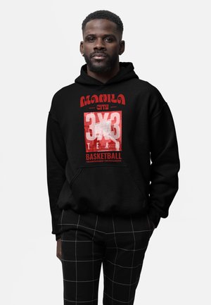 Homme portant un sweat à capuche noir avec le texte rouge « Manila City 3x3 Basketball Championship Tournament » et un pantalon noir à motif quadrillé blanc.