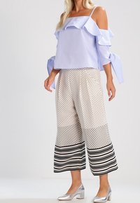 Světlomodrý top bez ramínek s volány, zkombinovaný s kalhotami s širokými nohavicemi s puntíky a pruhovanými okraji. Stříbrné boty outfit dotvářejí.