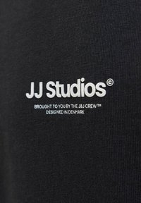 Fekete szövet sima textúrával, fehér hímzett felirattal: "JJ Studios," "A J&J Crew bemutatja," és "Tervezve Dániában."