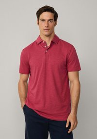 Kortärmad polo t-shirt i melerat rött tyg, med klassisk krage, treknappsknäppning och lätt oregelbunden textur.