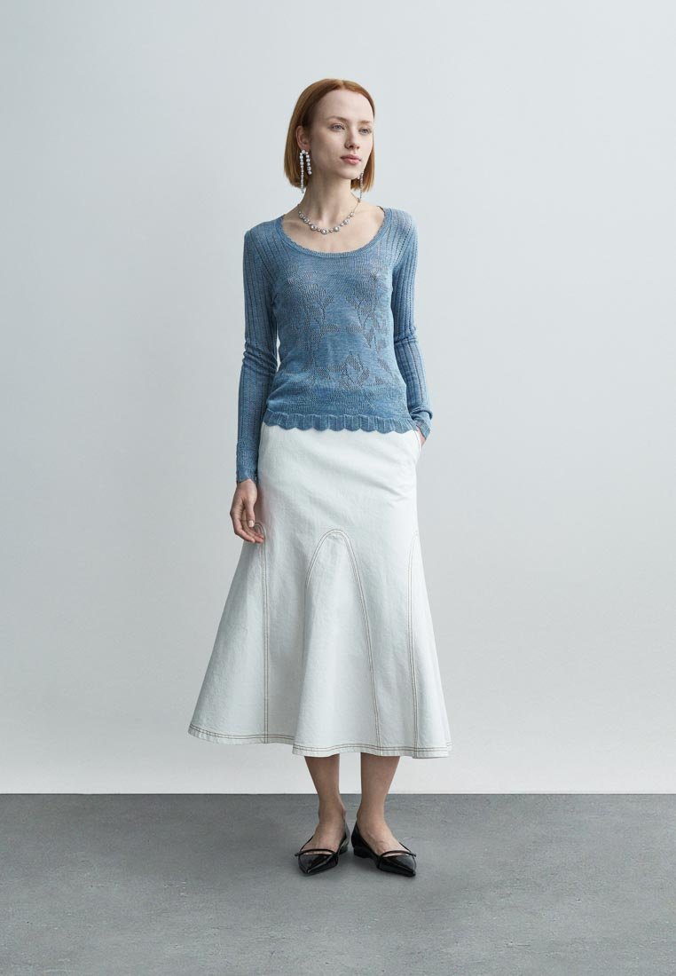 Haut à manches longues en tricot bleu clair avec motif texturé et ourlet festonné, associé à une jupe blanche ajustée avec des coutures apparentes.