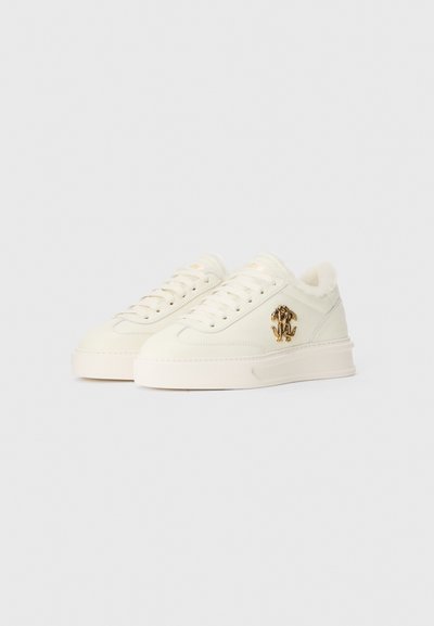 White sneakers with a textured surface, plush lining, and a gold logo accent on the side. Features lace-up design and rubber sole.