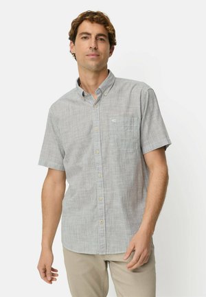 Mężczyzna w jasnoszarej koszuli z krótkim rękawem i kieszenią na piersi, stojący na białym tle.