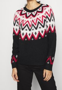 Strickpullover mit auffälligen Zickzack- und Diamantmustern in Rot, Weiß und Schwarz. Runder Ausschnitt und lange Ärmel. Weiche Textur.