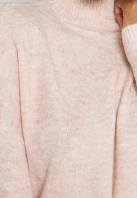 Helles rosa gestricktes Sweatshirt mit hochschließendem Kragen und weicher Textur, das ein dezentes gesprenkeltes Muster aufweist.