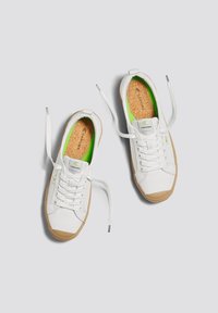 Scarpe da ginnastica bianche in tela con soletta verde, fodera in sughero e suole in gomma. Presentano punta rotonda, lacci piatti e dettagli di branding sottili.