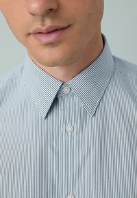 Hellblau und weiß gestreiftes Hemd mit spitzem Kragen, drei Knöpfen und einer glatten Baumwolltextur. Nahaufnahme.